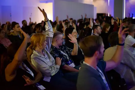 An audience of people raising their hands during a talk.