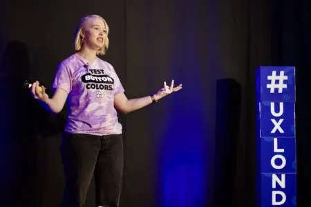 A woman speaking on stage at UX London with her arms held out.