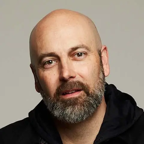 A shaven-headed man with a beard looking right at you with his tilted slightly to one side.