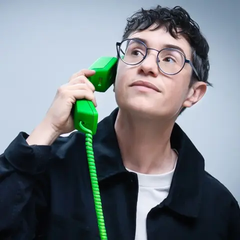 Lou wearing a jacket and glasses holding an old-fashioned green telephone.