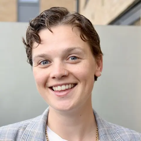 A young person with short hair smiling wearing a jacket.