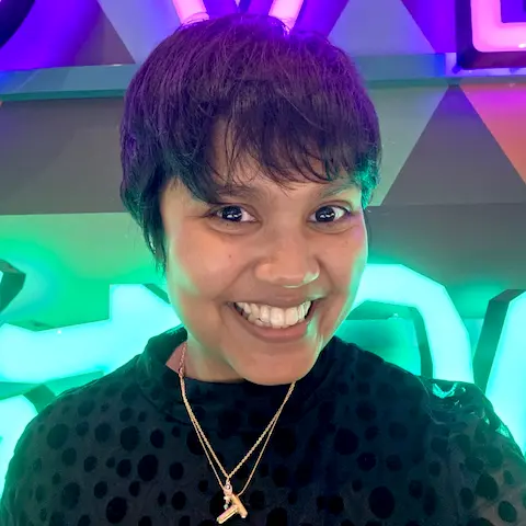 A smiling young woman with short hair in front of neon lights.