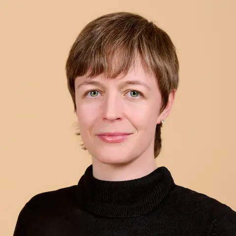 A woman with short hair and a dark top against a pastel background.